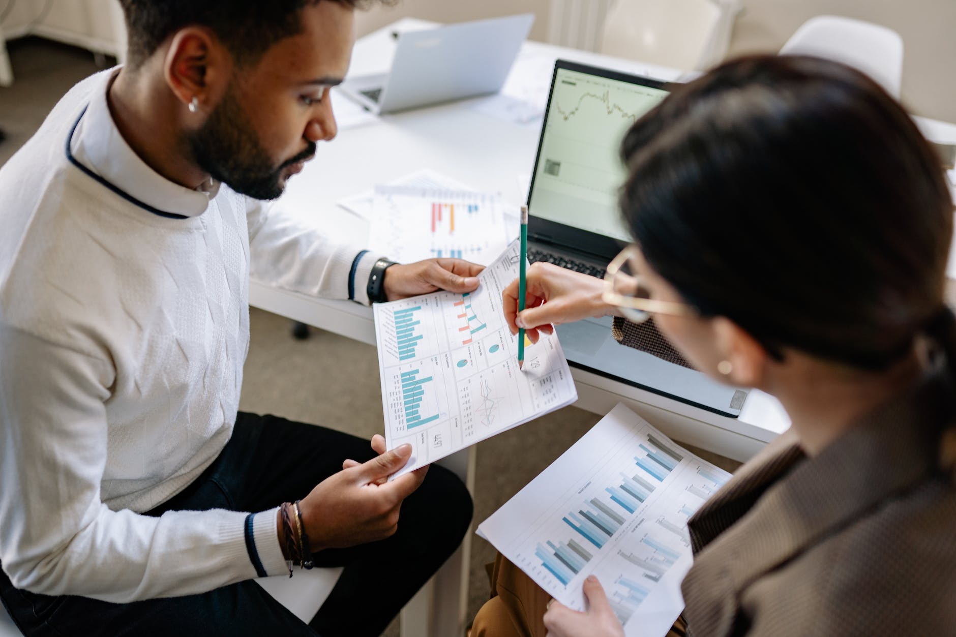 A man and a woman in a discussion examining and performing data analytics with an open laptop on the table.
