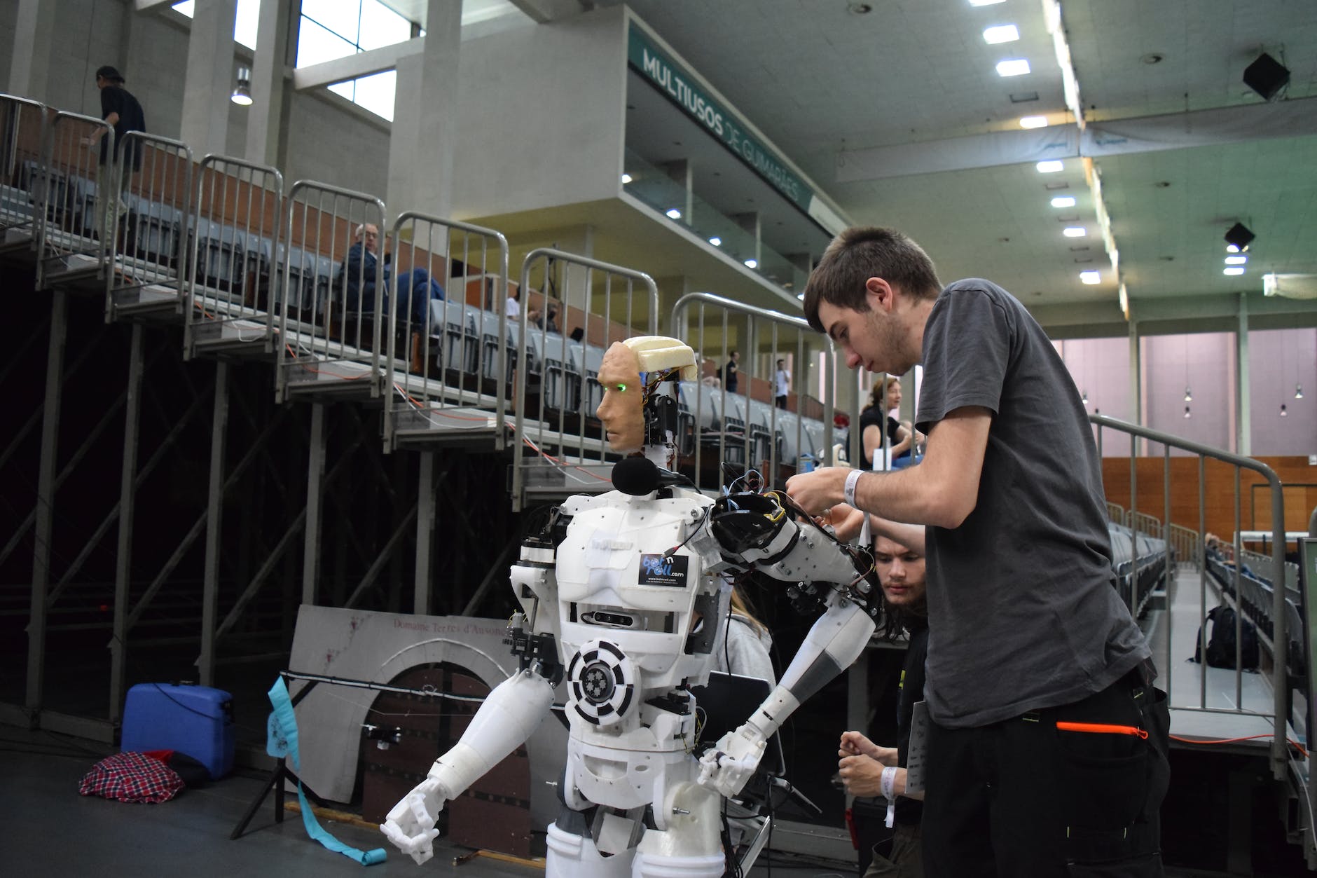 Man fixing a human-like robot inside a sports center. 